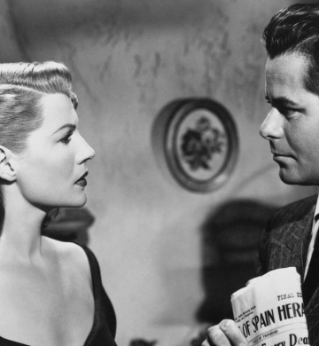 A woman is looking at a man who is holding a newpaper